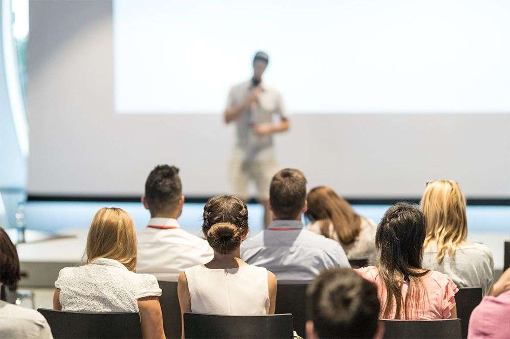  A person presenting to an audience. The audience are in focus and the presenter is out of focus.